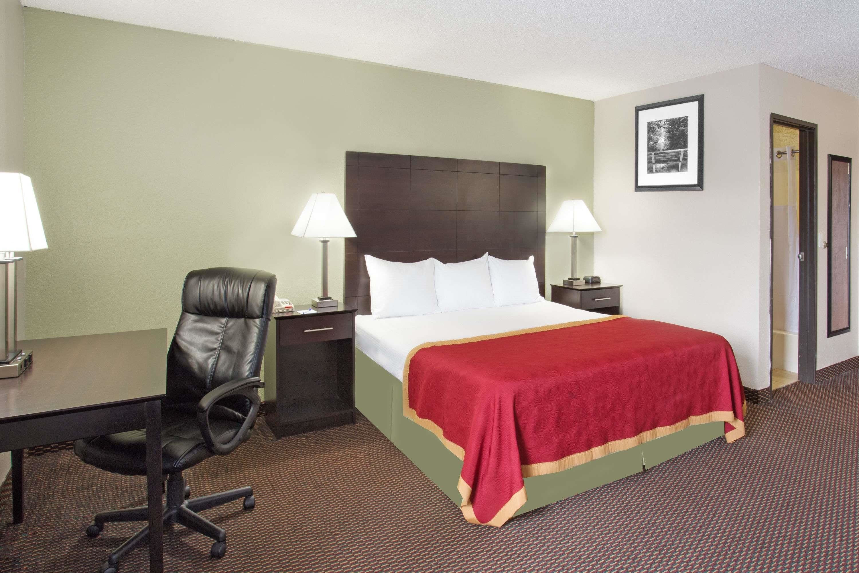 A hotel room with a bed, a desk, a chair, two bedside lamps, and a framed picture on the wall.