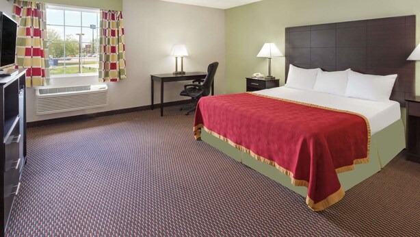 Una habitación de hotel con una cama grande, un escritorio, una silla, un televisor y una ventana con cortinas.