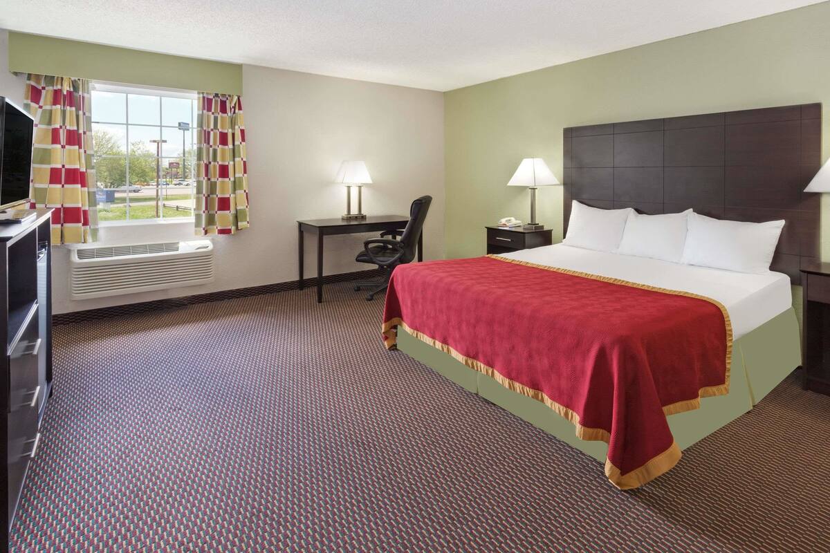 A hotel room with a large bed, a desk, a chair, a TV, and a window with curtains.