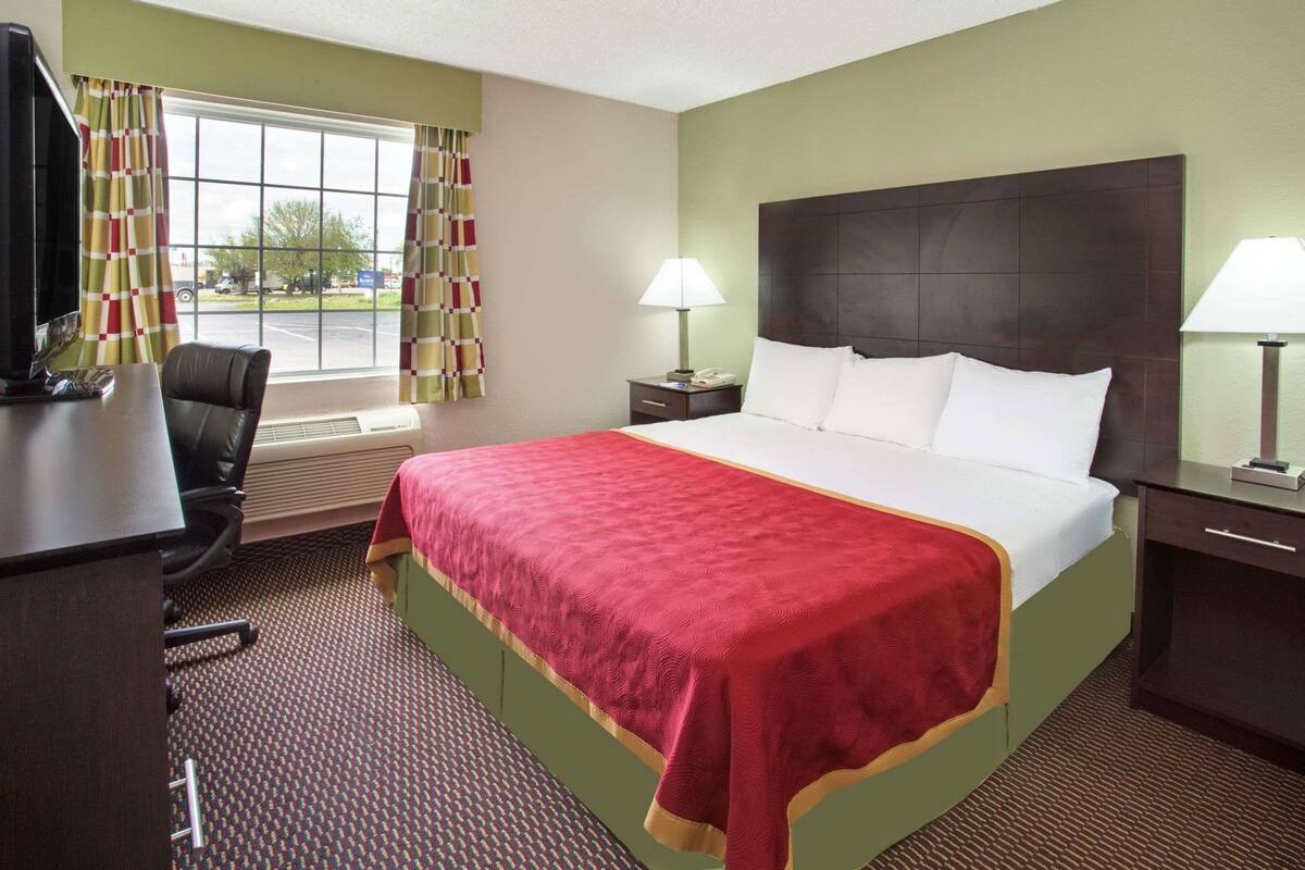 A hotel room with a bed, desk, chair, two bedside lamps, and a window with curtains.