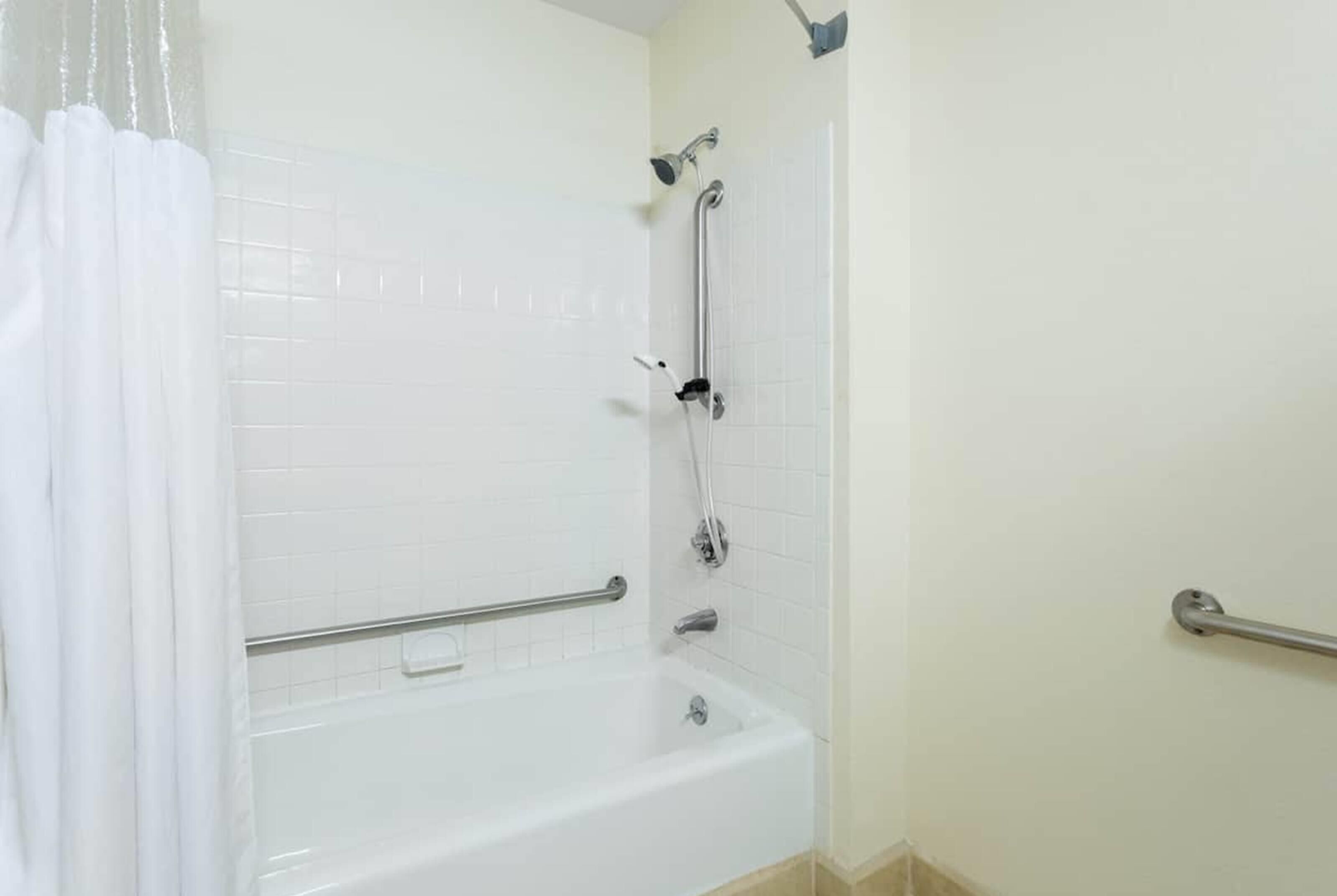 Een badkamer met een wit bad, een douche met een handdouche en een handgreep.