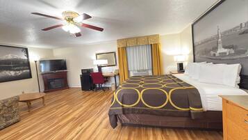 A hotel room with a bed, a desk, a chair, a television, a fireplace, and a ceiling fan.