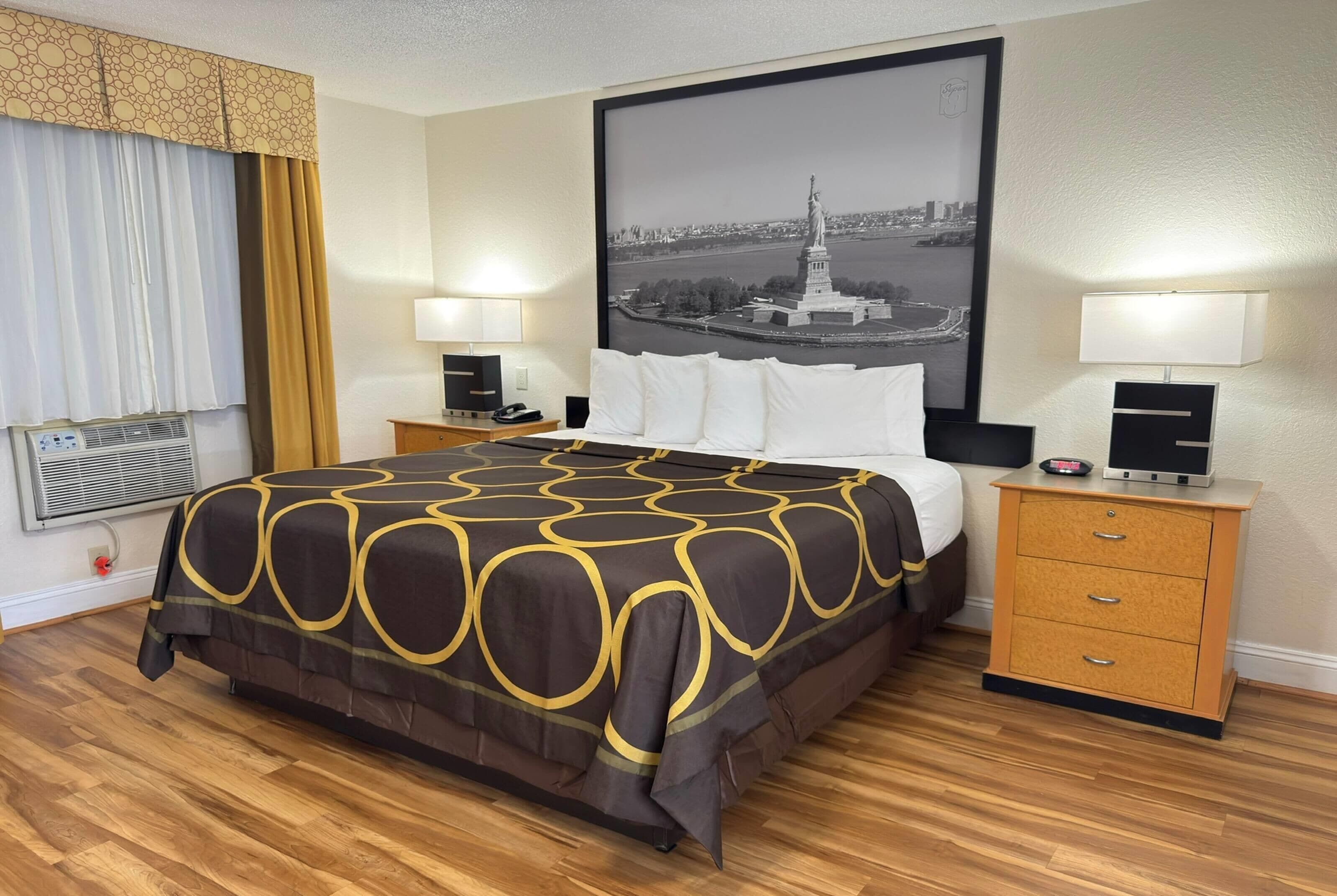 A hotel room with a large bed, two bedside tables with lamps, a framed picture on the wall, and a window with curtains.