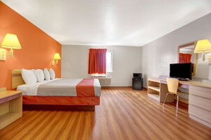Quarto de hotel com cama, escrivaninha, cadeira, televisão e janela com cortinas.