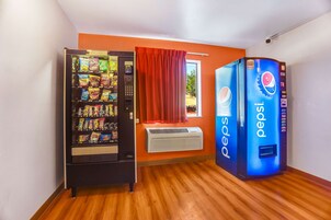 Quarto com máquina de vendas de lanches, uma grande máquina de Pepsi e uma janela com cortinas vermelhas.