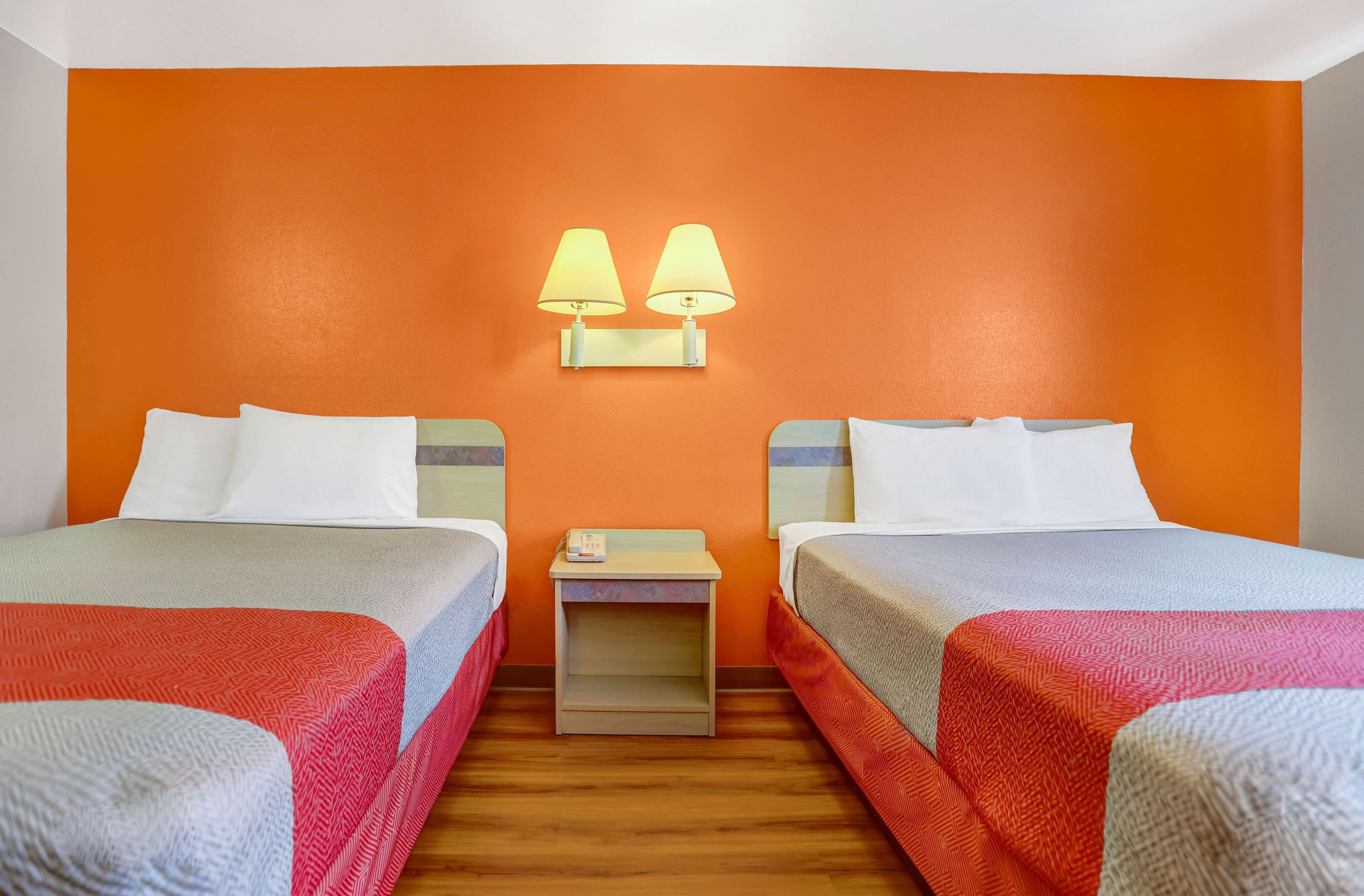 A hotel room with two beds, a nightstand, and two wall-mounted lamps.