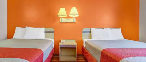 A hotel room with two beds, a nightstand, and two wall-mounted lamps.