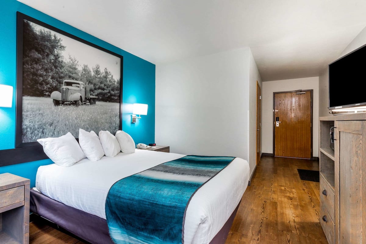 Habitación de hotel con una cama grande, televisión, un armario de madera y una puerta que da a otra habitación.