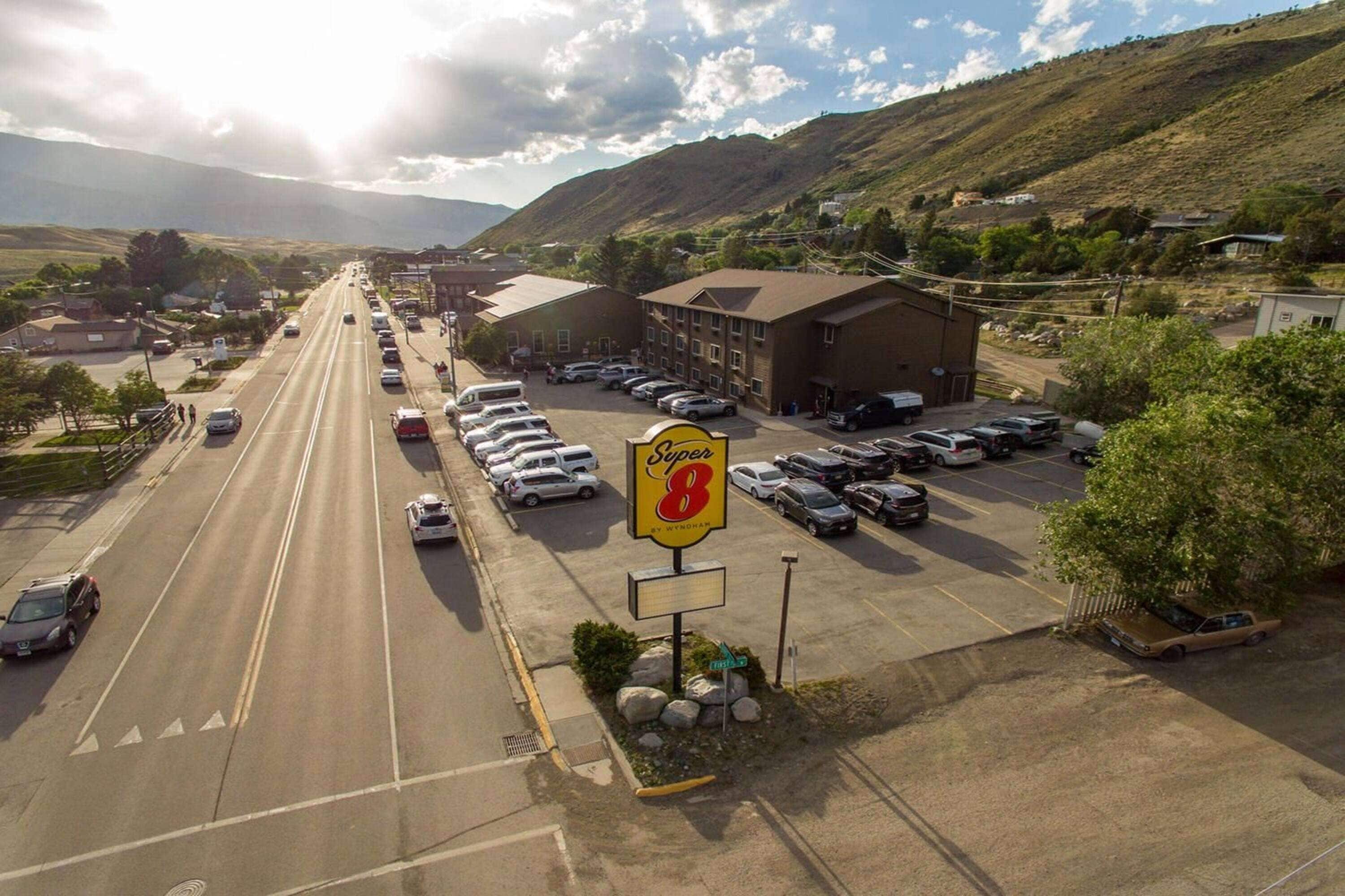 A Super 8 motel with a large parking lot, a main building, and a mountain backdrop.