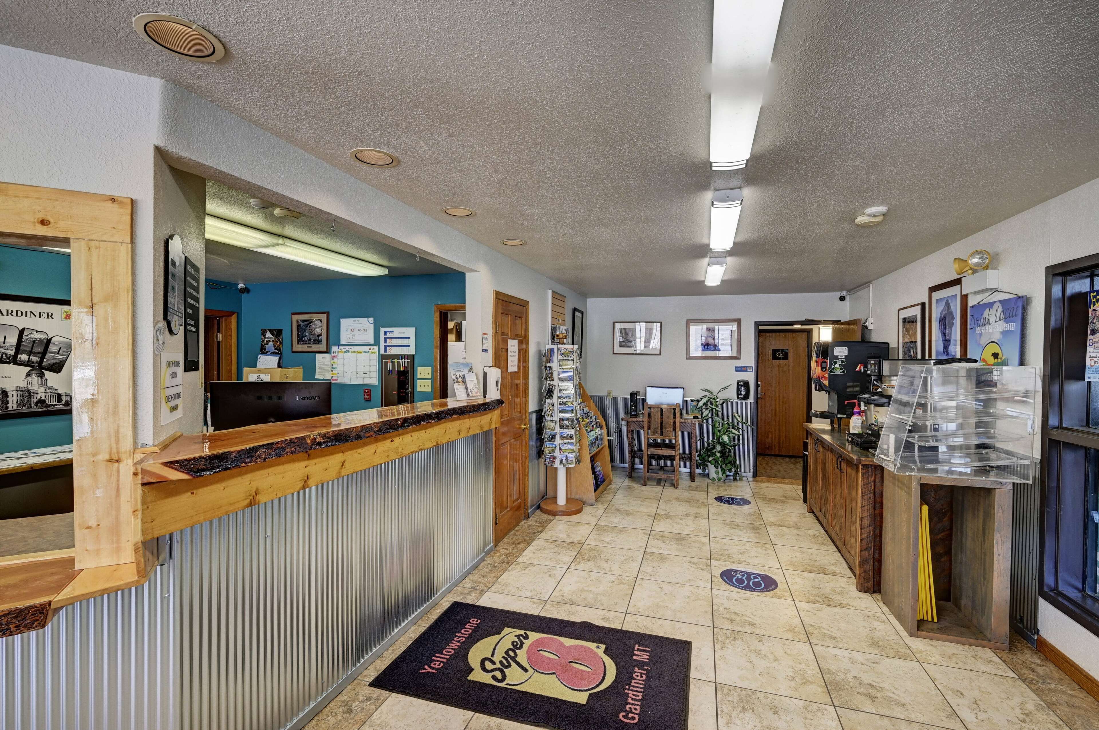 A reception area with a wooden counter, a reception desk, a wall-mounted phone, framed pictures, a bulletin board, and a coffee station.