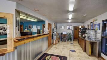 A reception area with a wooden counter, a reception desk, a wall-mounted phone, framed pictures, a bulletin board, and a coffee station.