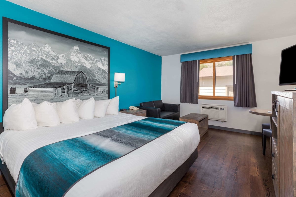 Habitación de hotel con una cama grande, un escritorio, una silla, un televisor y una ventana con cortinas.