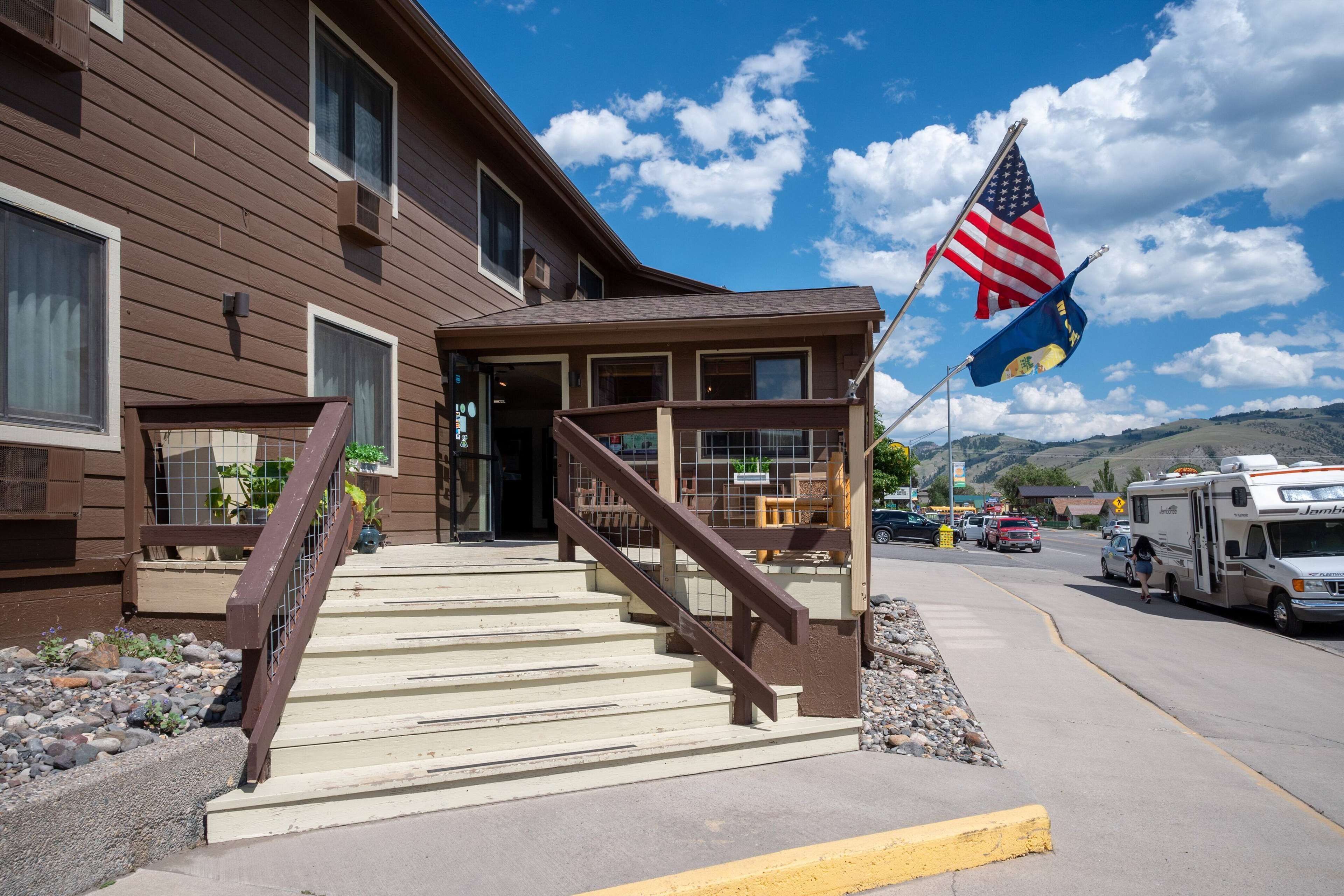 A two-story building with a staircase leading to the entrance, an American flag, and a parked RV on the street.