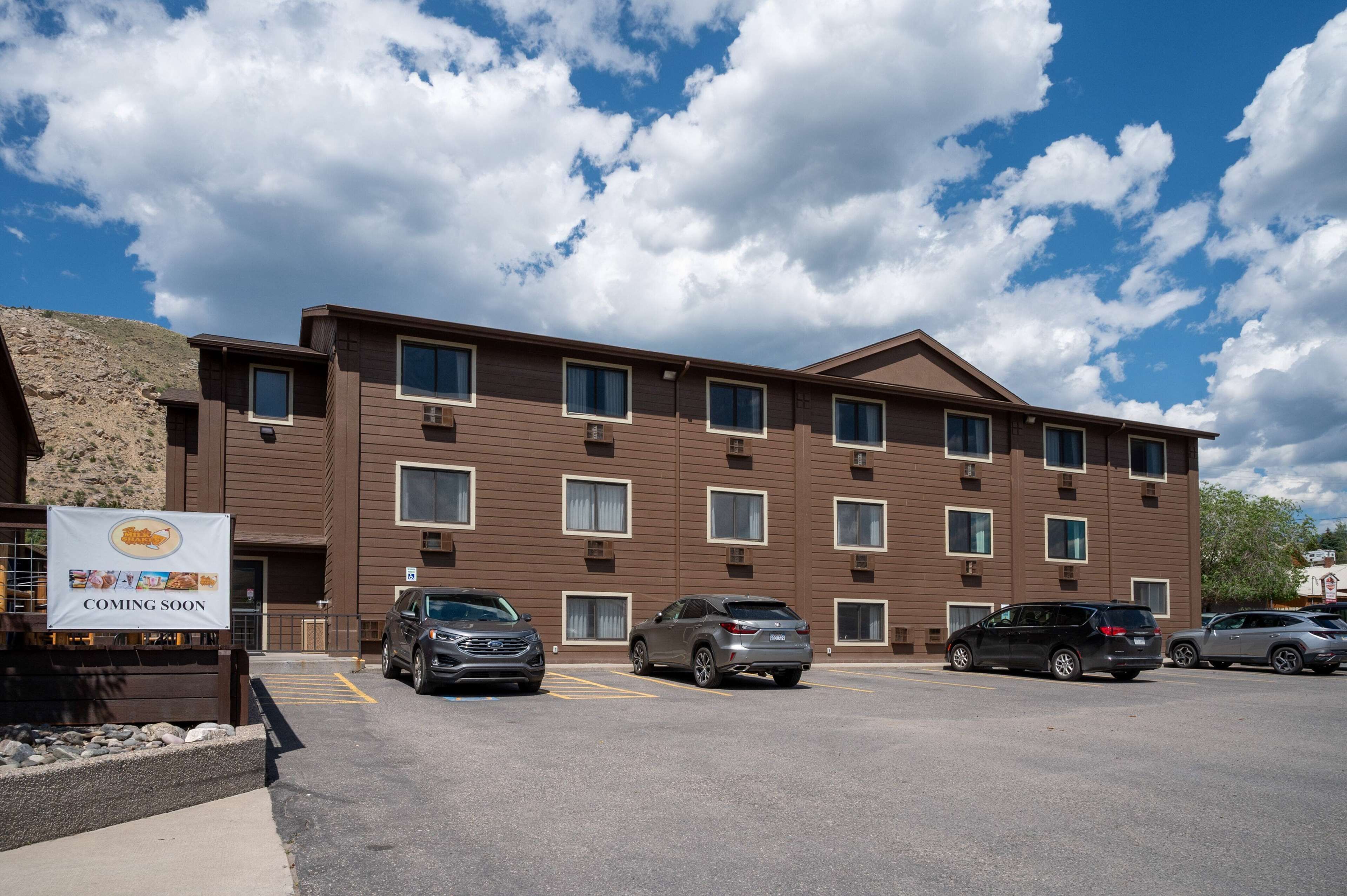 A multi-story building with a brown facade, several windows, and a parking lot with cars.