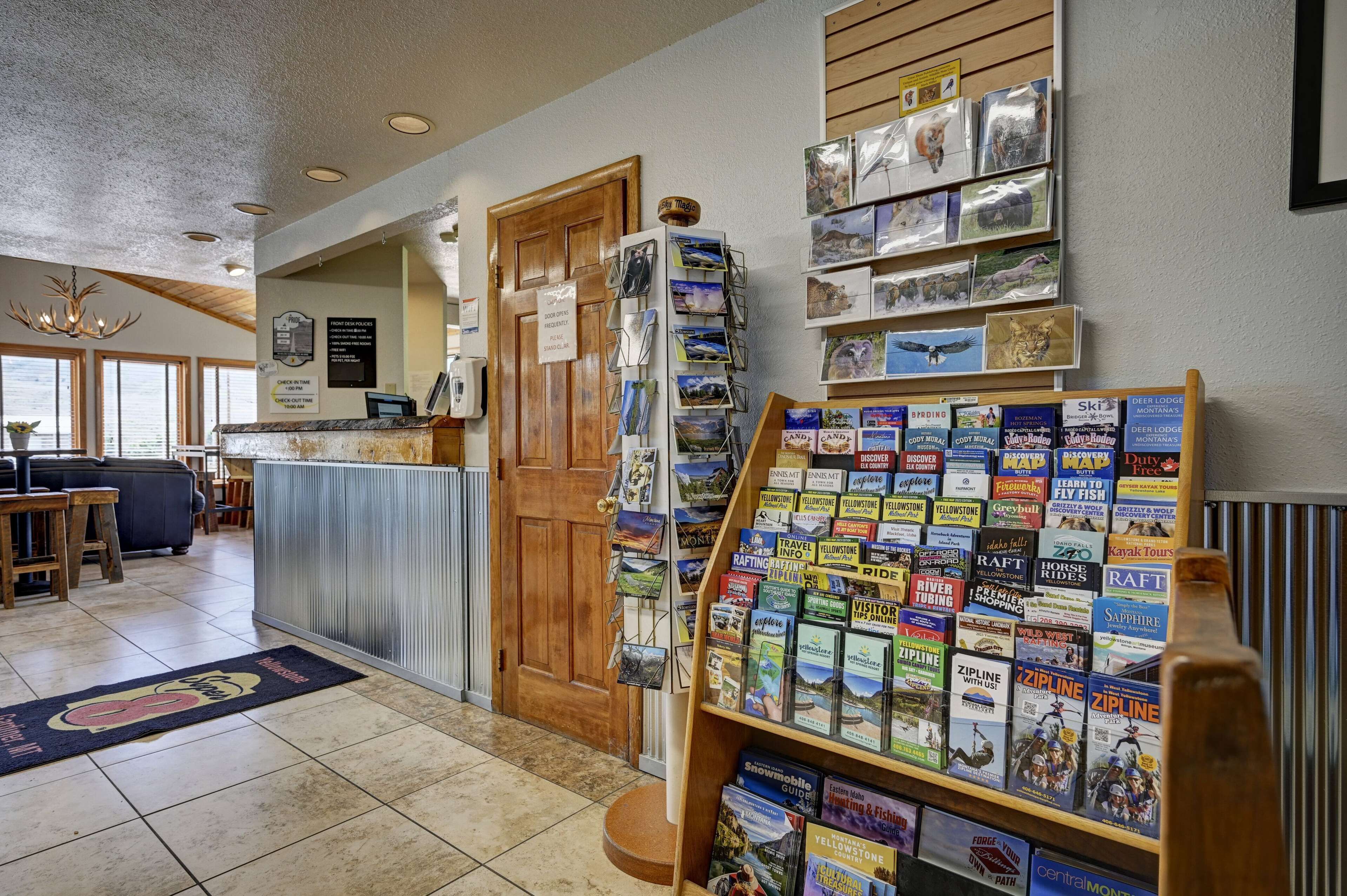 A reception area with a wooden desk, a bulletin board with travel brochures, and a sign indicating check-in times.