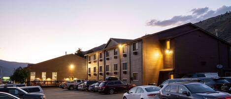 A parking lot with several cars, a building with multiple windows and a flat roof, and a mountain in the background.