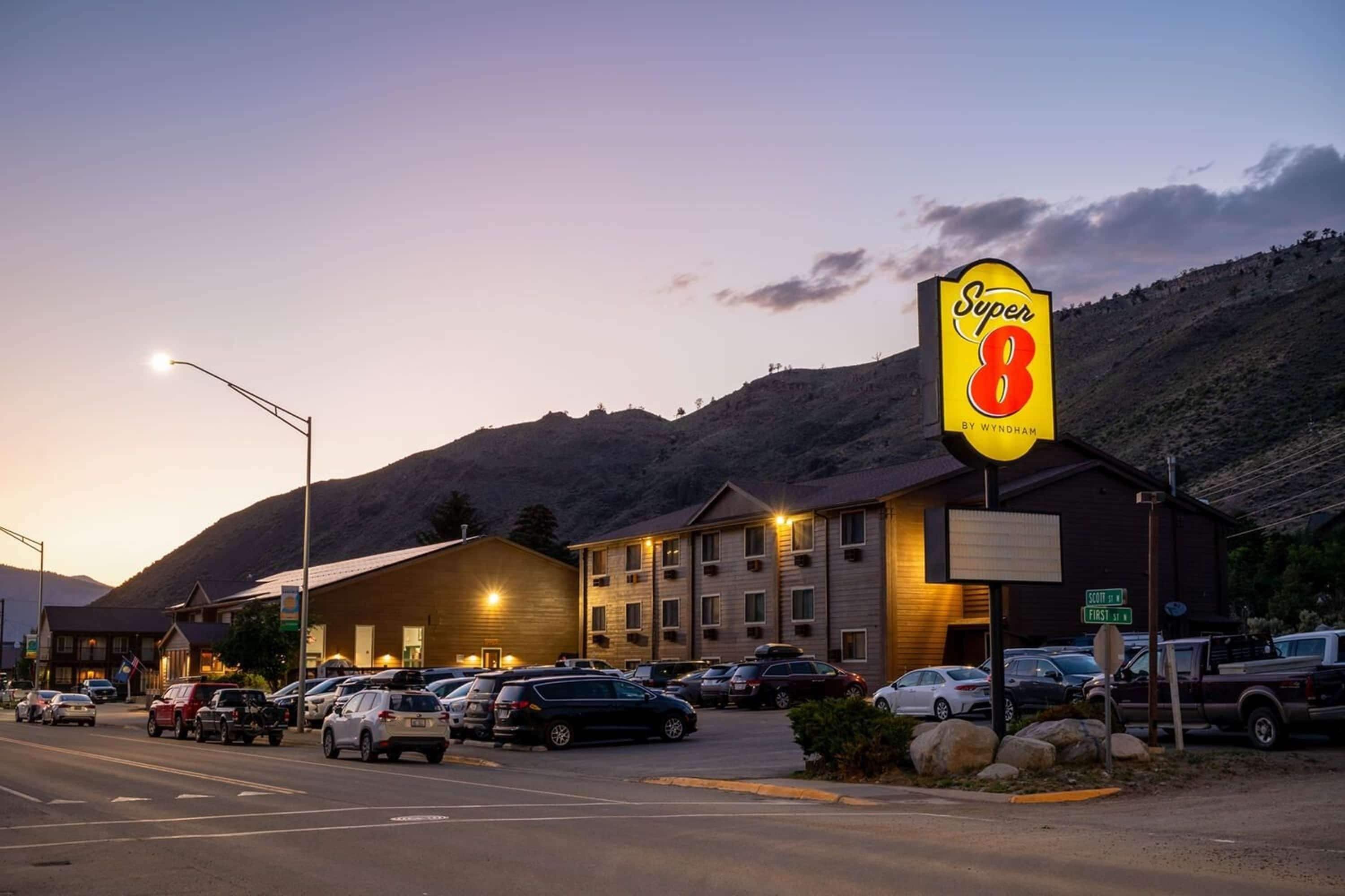 A Super 8 motel with a parking lot, a mountain backdrop, and a street lamp.