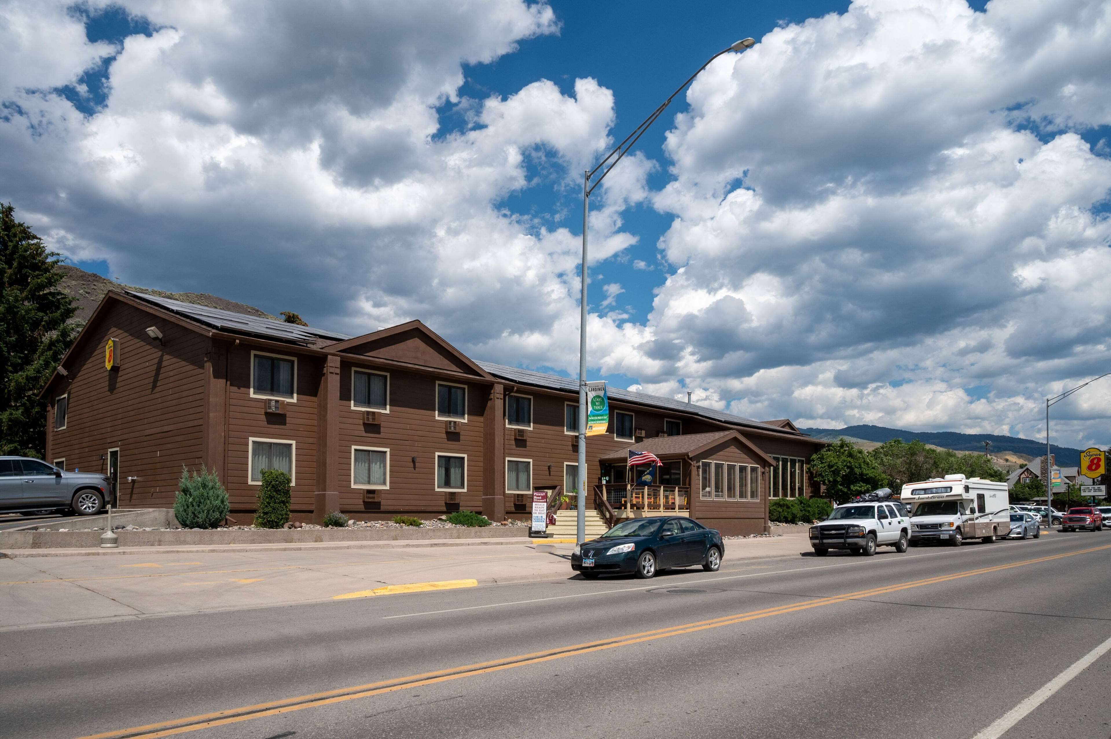 A brown building with a sign indicating it is a hotel. There is a street with cars and a truck, and a mountain range in the background.