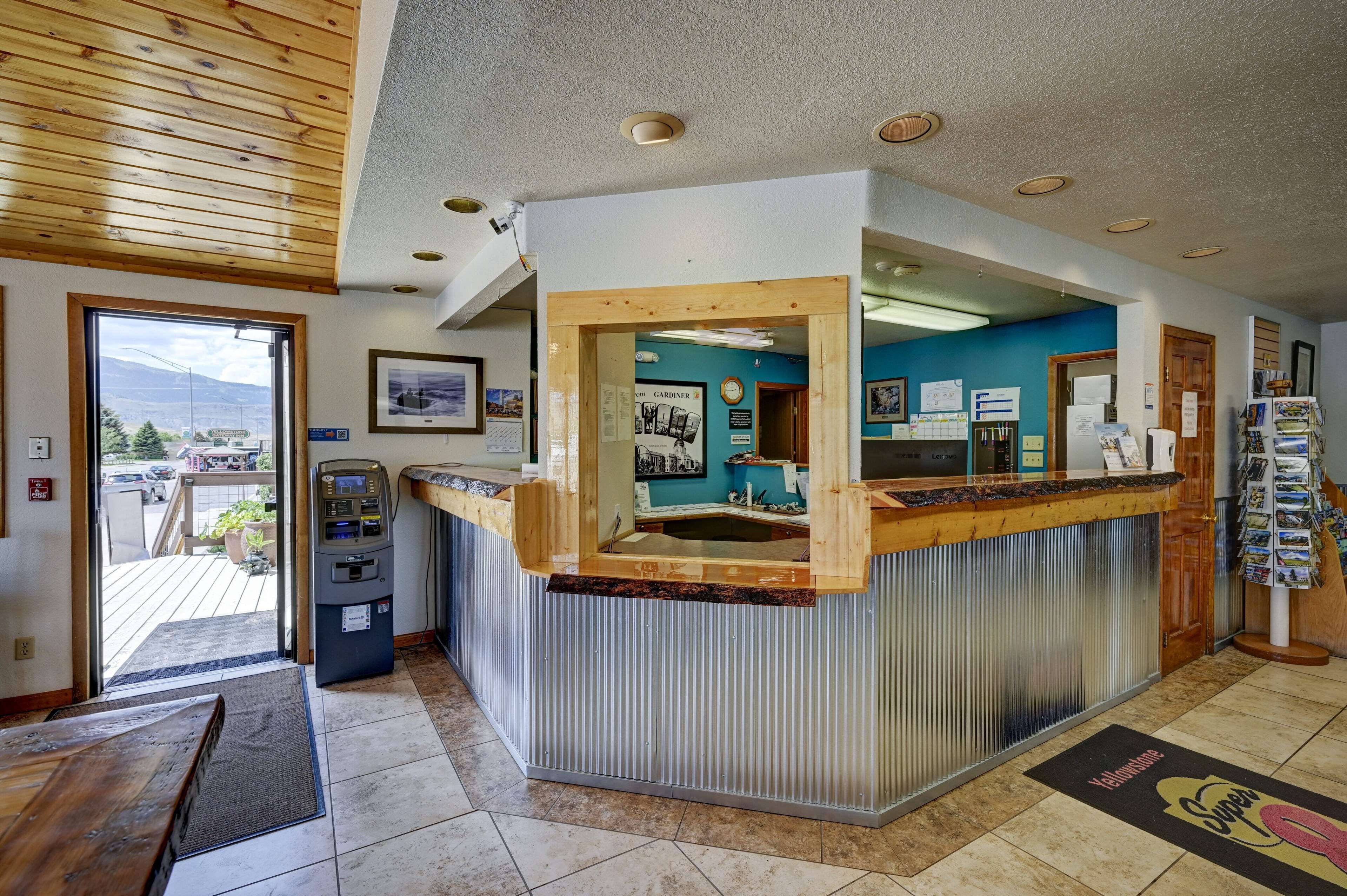 A reception area with a wooden counter, a view of the mountains through the window, and a parking lot visible outside.