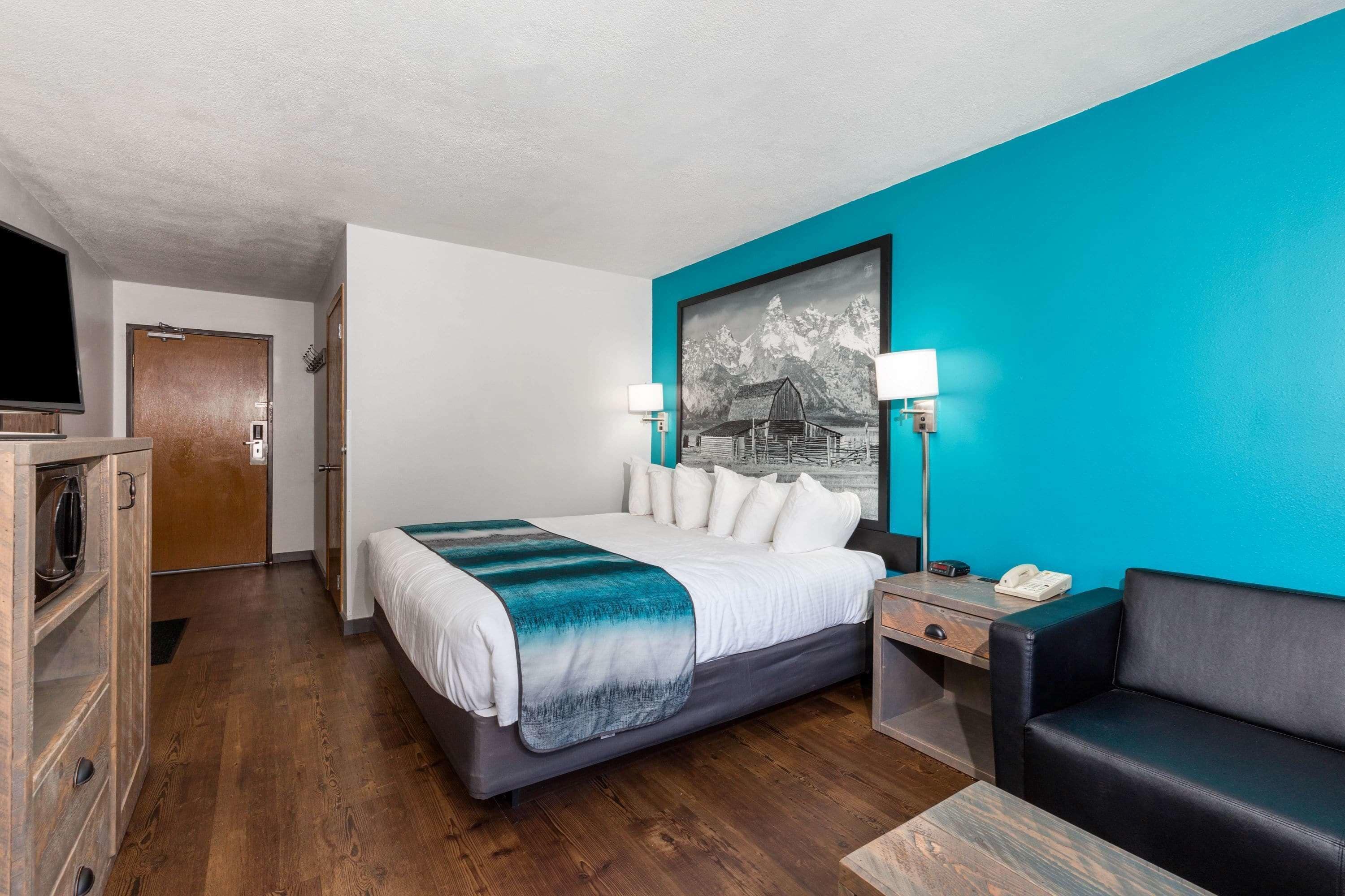 A hotel room with a bed, a desk, a chair, a TV, and a painting on the wall.