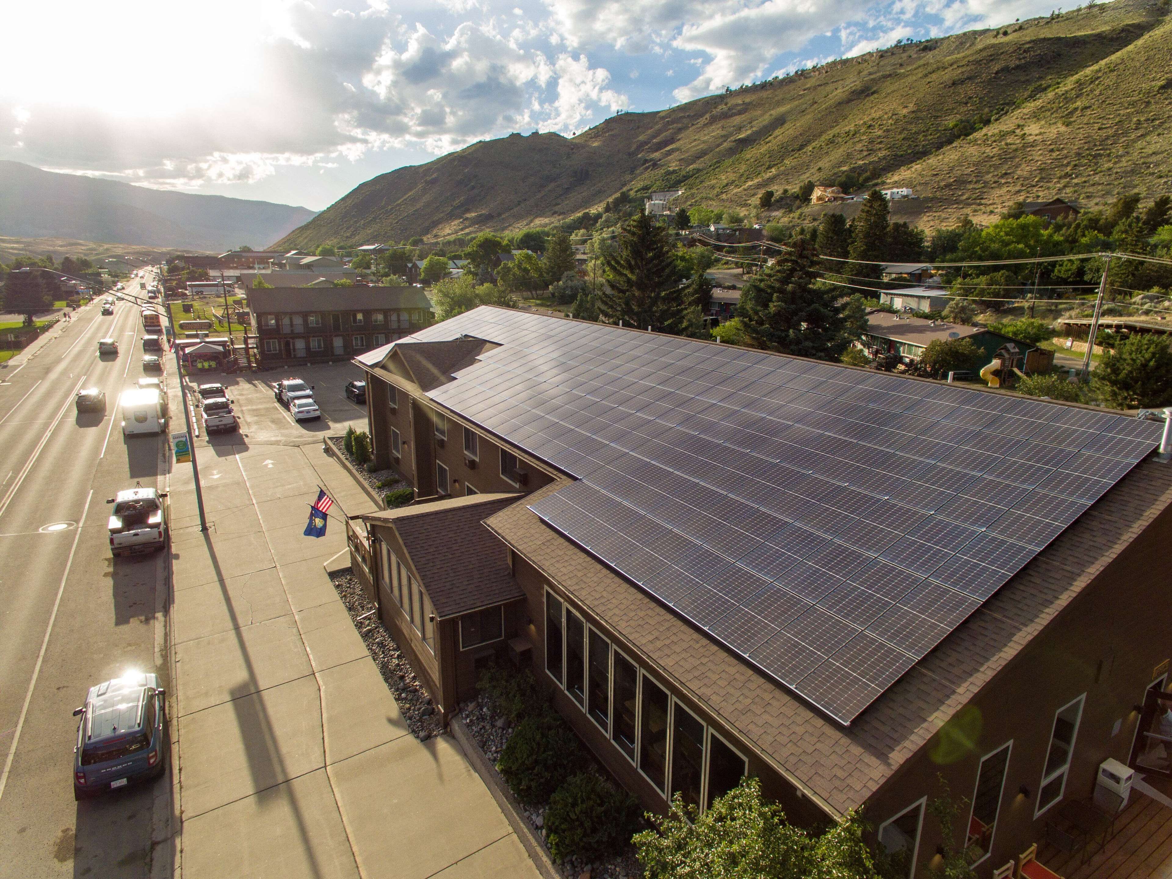 Un edificio con techo de paneles solares, estacionamiento y una carretera con vehículos.