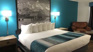 Een hotelkamer met een groot bed, twee bedlampen, een bruine leren fauteuil en een berglandschap op de muur.