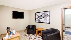 Una habitación pequeña con televisión, un cuadro enmarcado, cafetera y dos sillas.
