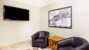 Sala de estar con dos sillones de cuero negro, una mesa de centro de madera, un televisor de pantalla plana montado en la pared y un letrero de bienvenida enmarcado.