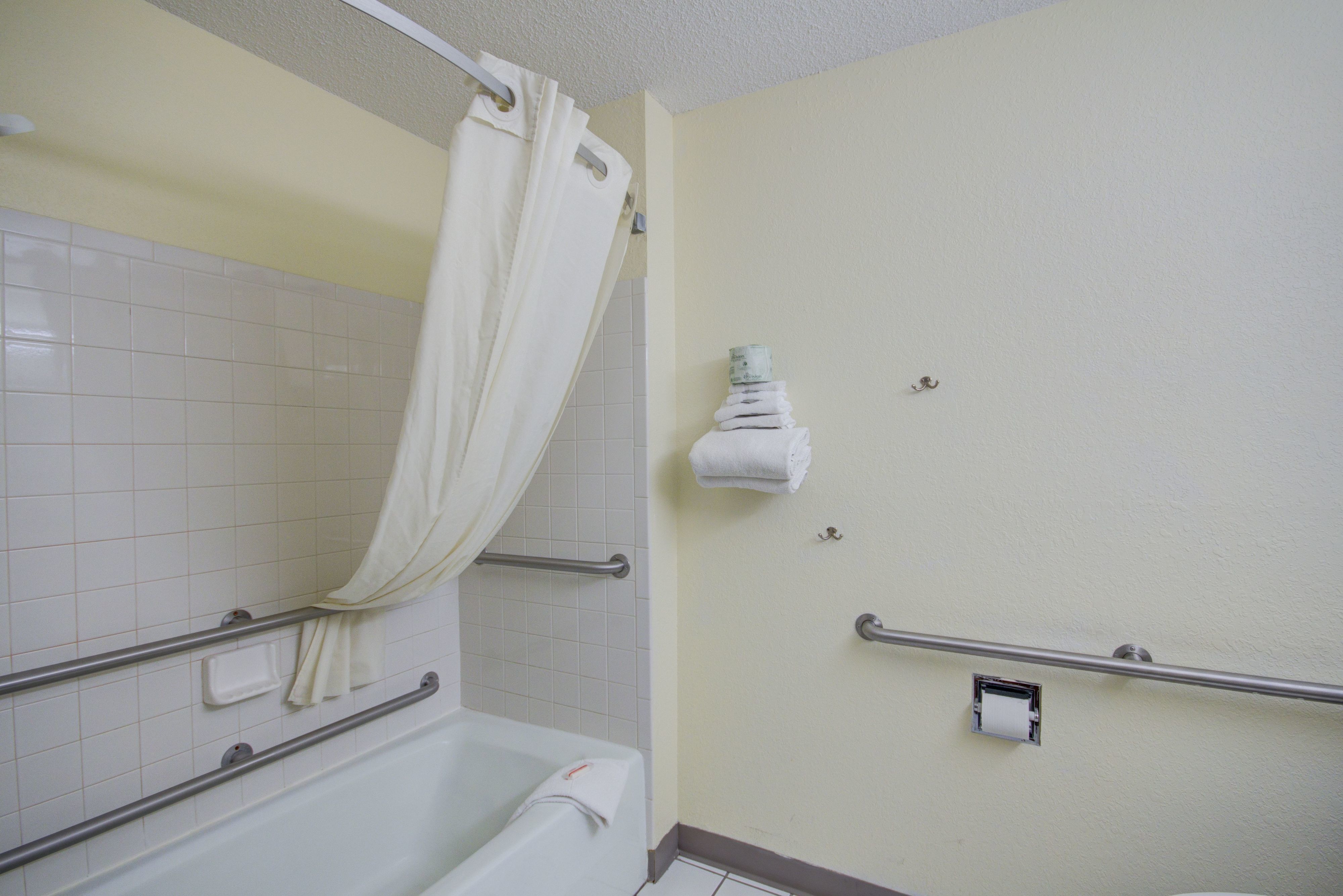 Une salle de bain avec une baignoire blanche, un rideau de douche, un porte-serviettes et un sèche-mains.