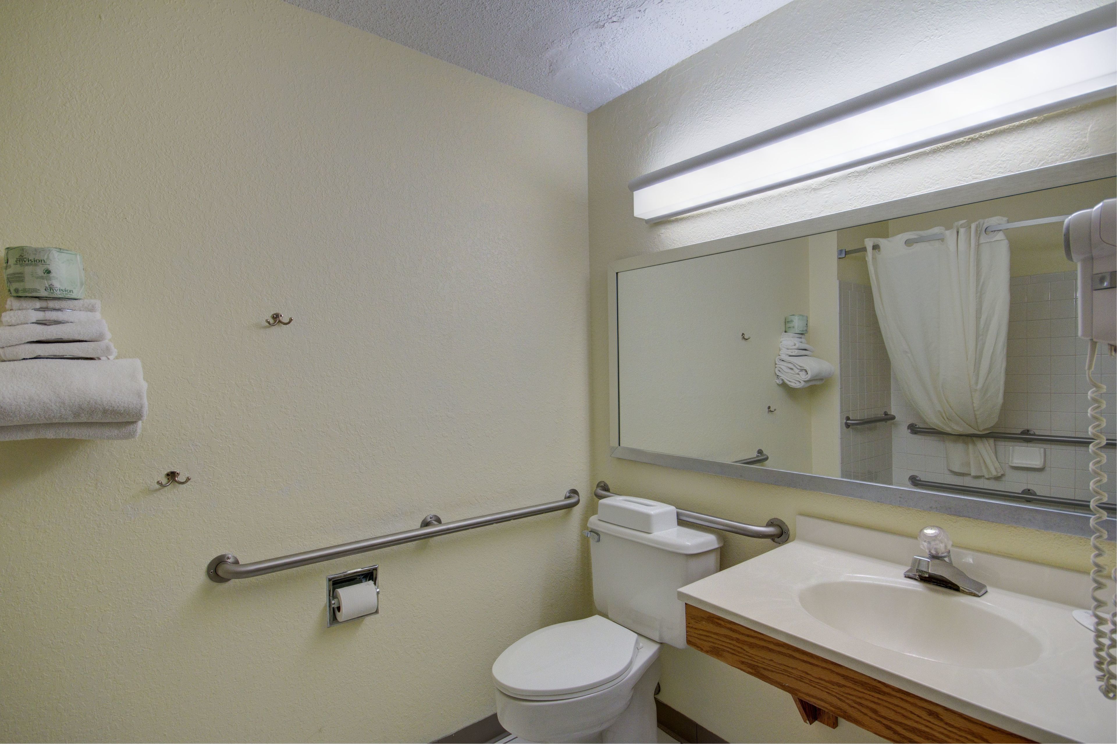 A bathroom with a toilet, sink, and mirror. There are handrails on the walls and a towel rack with towels.