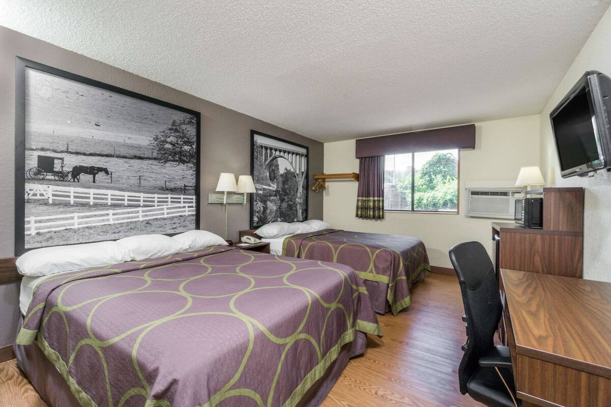 Ein Hotelzimmer mit zwei Betten, einem Schreibtisch, einem Fernseher und großen Fenstern.