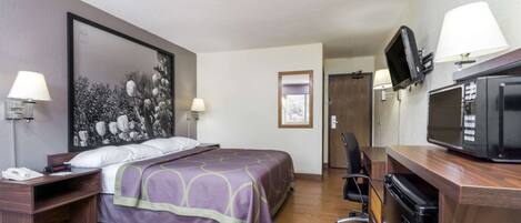 Une chambre d’hôtel comprenant un lit, des tables de chevet, un bureau avec un micro-ondes et une télévision.
