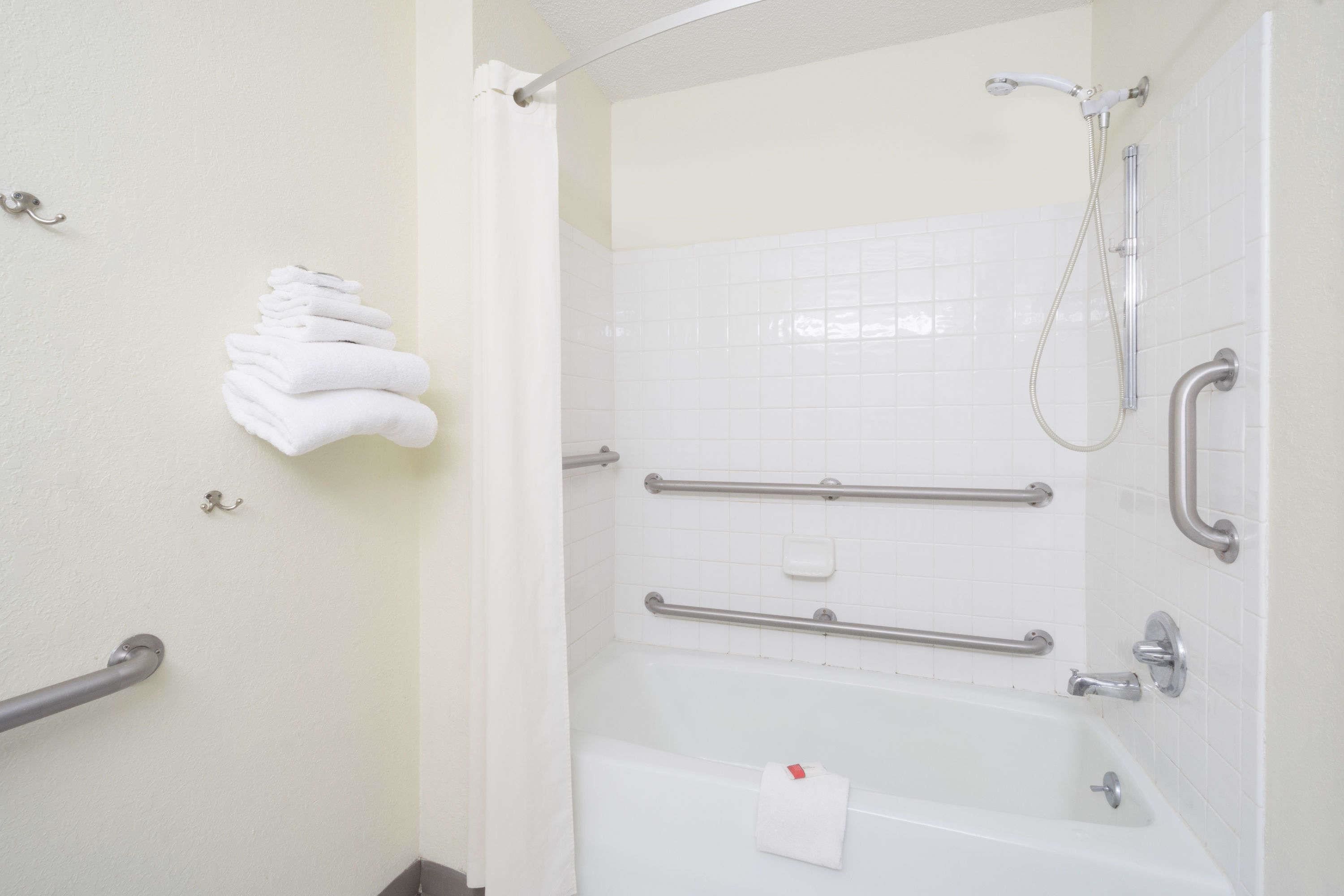 A bathroom with a bathtub, grab bars, a showerhead, and a towel rack.