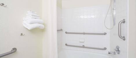 A bathroom with a bathtub, grab bars, a showerhead, and a towel rack.