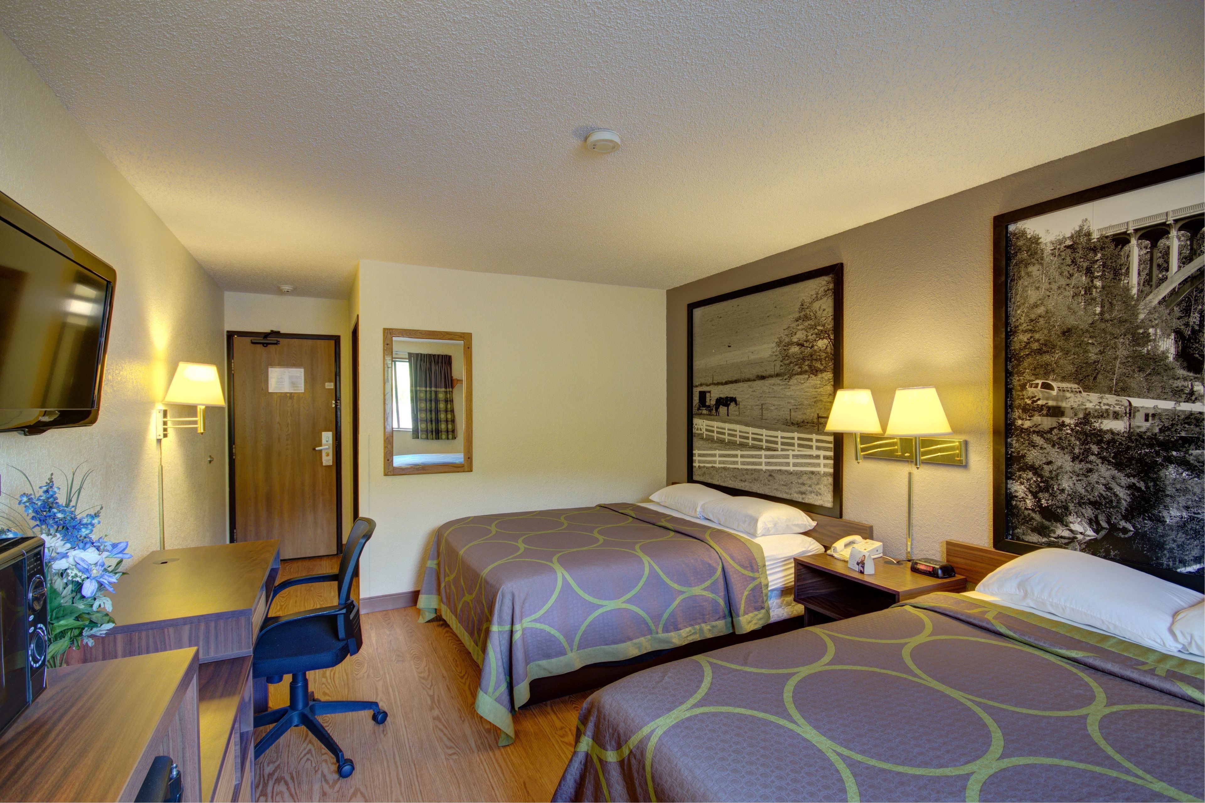 Habitación de hotel con dos camas, un escritorio, una silla, un televisor y un cuadro en la pared.