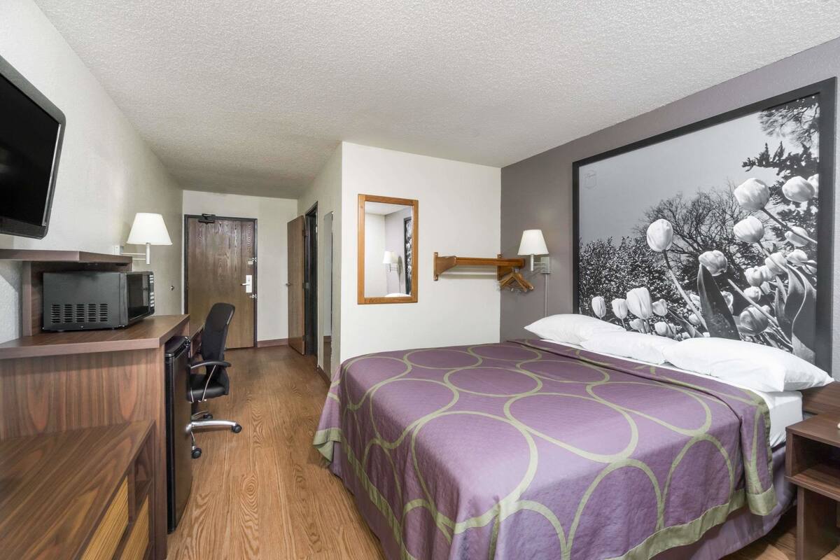 Ein Hotelzimmer mit einem Bett, einem Schreibtisch mit Computer, einem Sessel und einem Fernseher.
