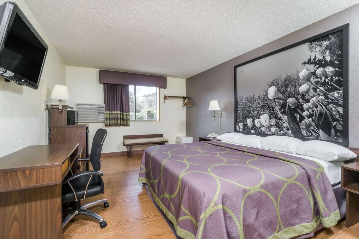 Ein Hotelzimmer mit Bett, Schreibtisch, Stuhl, Fernseher und einem Kunstwerk an der Wand.