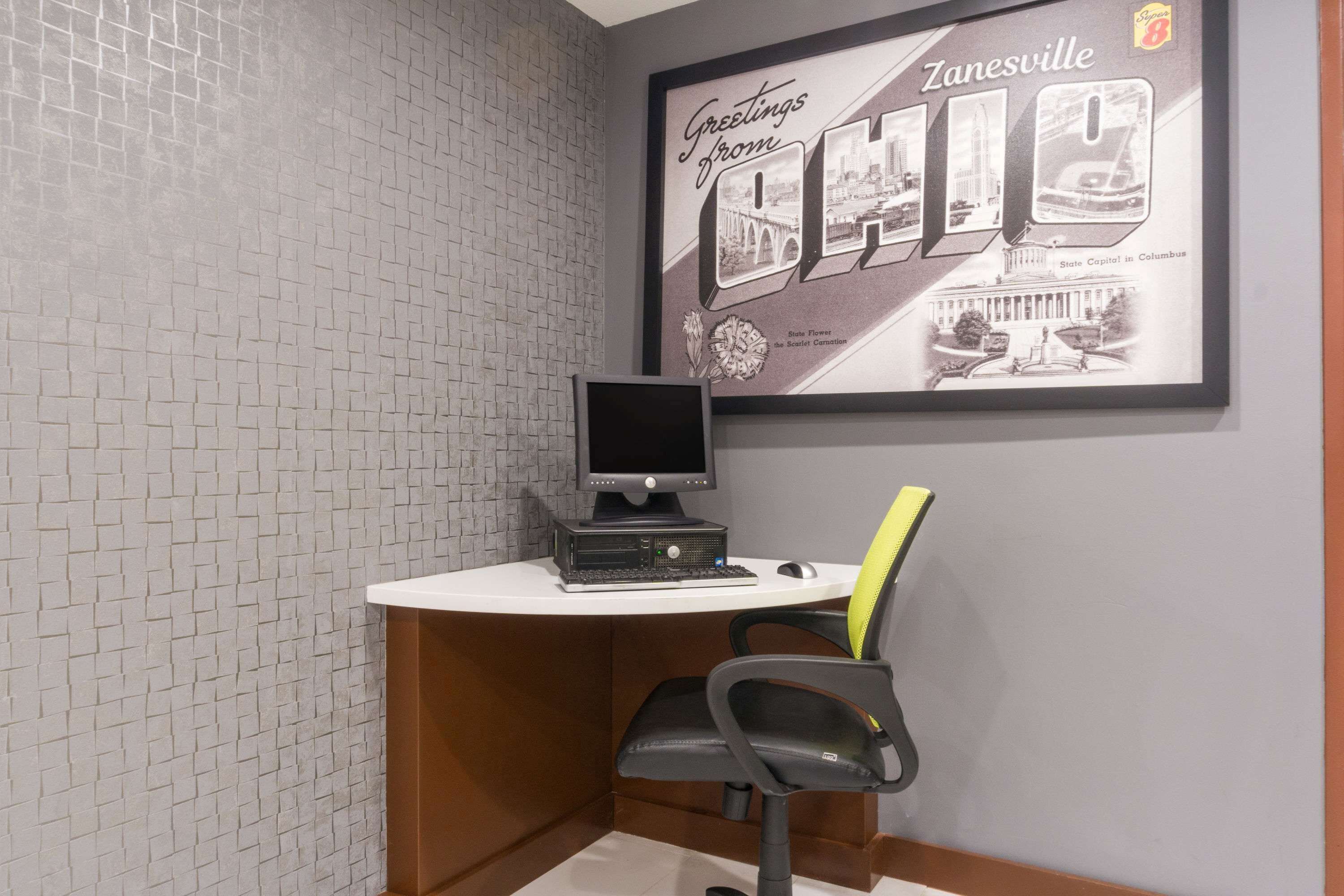 A small office space with a computer on a desk, a framed picture of Zanesville on the wall, and a brick-patterned wall.