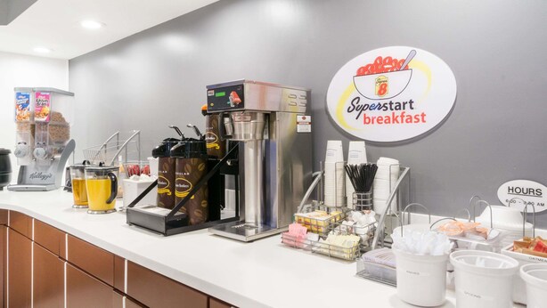 A breakfast station with a coffee machine, coffee cups, and various breakfast items. - Super 8 by Wyndham Zanesville (Zanesville)