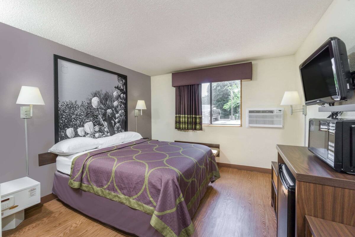 Ein Hotelzimmer mit einem Bett, einem Fernseher, einem Schreibtisch und einem Fenster mit Vorhängen.