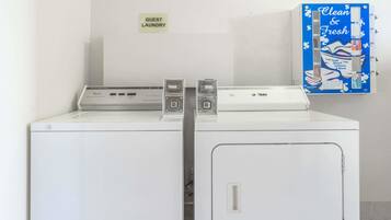 A laundry area with two washing machines, a sign indicating guest laundry, and a blue sign advertising "Clean & Fresh" services.