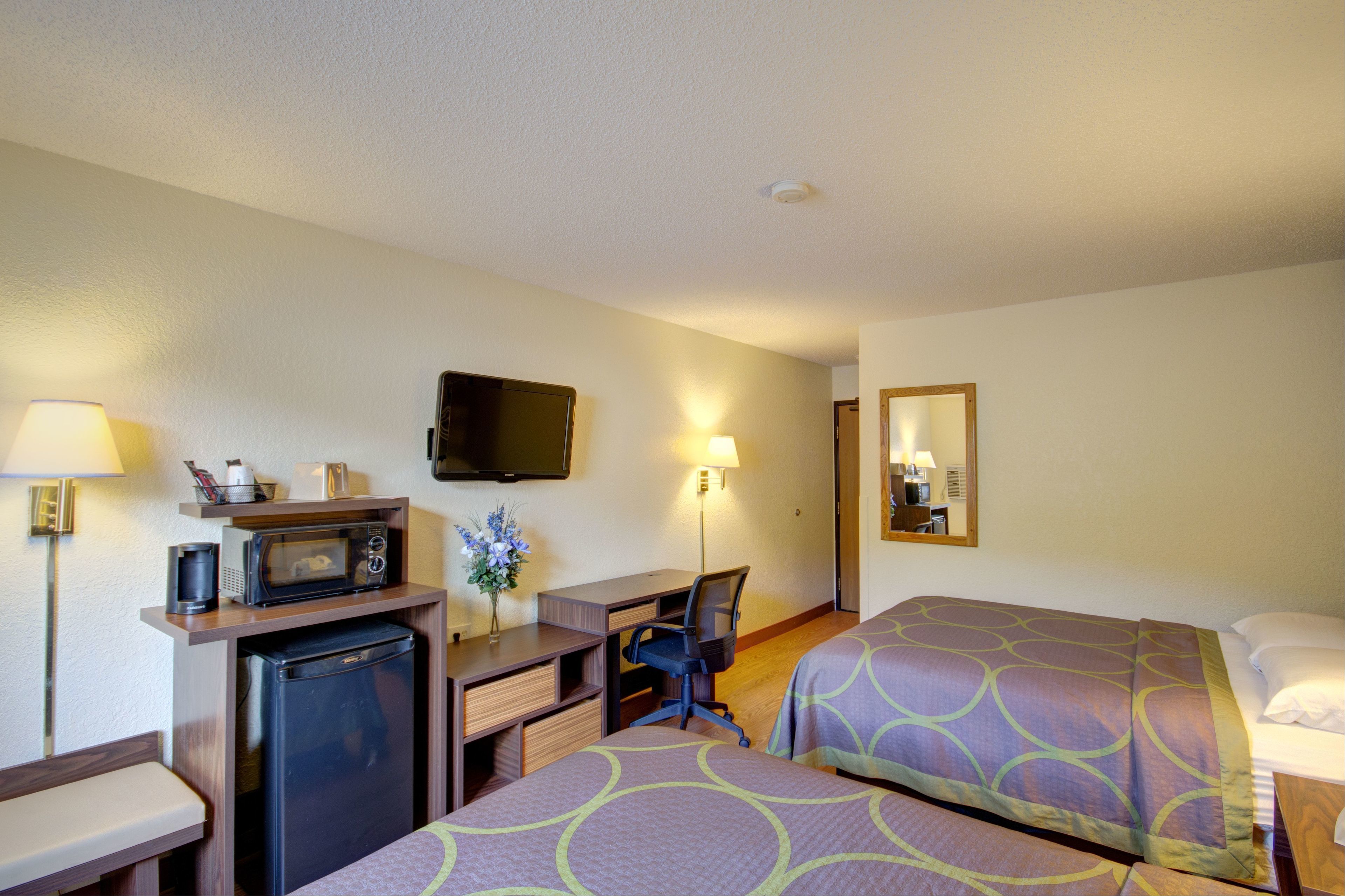 A hotel room with two beds, a desk with a computer, a microwave, and a refrigerator.