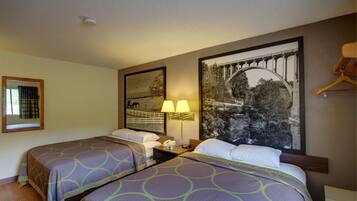 A hotel room with two single beds, a nightstand with a lamp, a large framed picture of a bridge, and a wooden hanger on the wall.