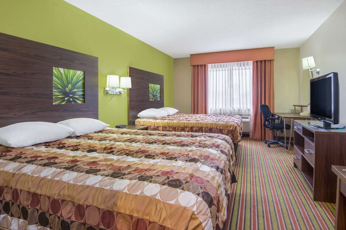 Une chambre d’hôtel avec deux lits, un bureau, une télévision et une fenêtre avec des rideaux.