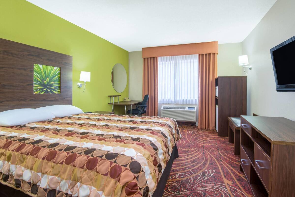 Une chambre d’hôtel avec un grand lit, un bureau, une chaise, une télévision et une fenêtre avec des rideaux.