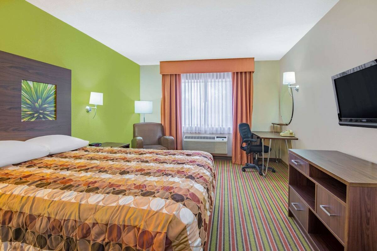 Une chambre d’hôtel équipée d’un lit, d’un bureau, d’une chaise, d’une télévision et d’une fenêtre avec des rideaux.