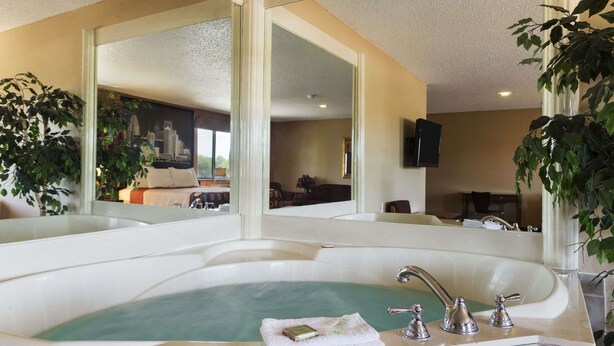 A large bathtub with a greenish water feature, a white towel, and a bottle of soap. - Super 8 by Wyndham Taylor/Detroit Area (Taylor)