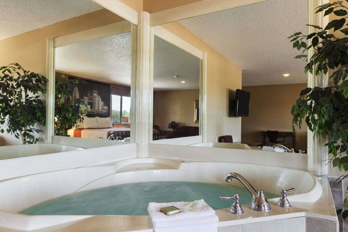 A large bathtub with a greenish water feature, a white towel, and a bottle of soap.