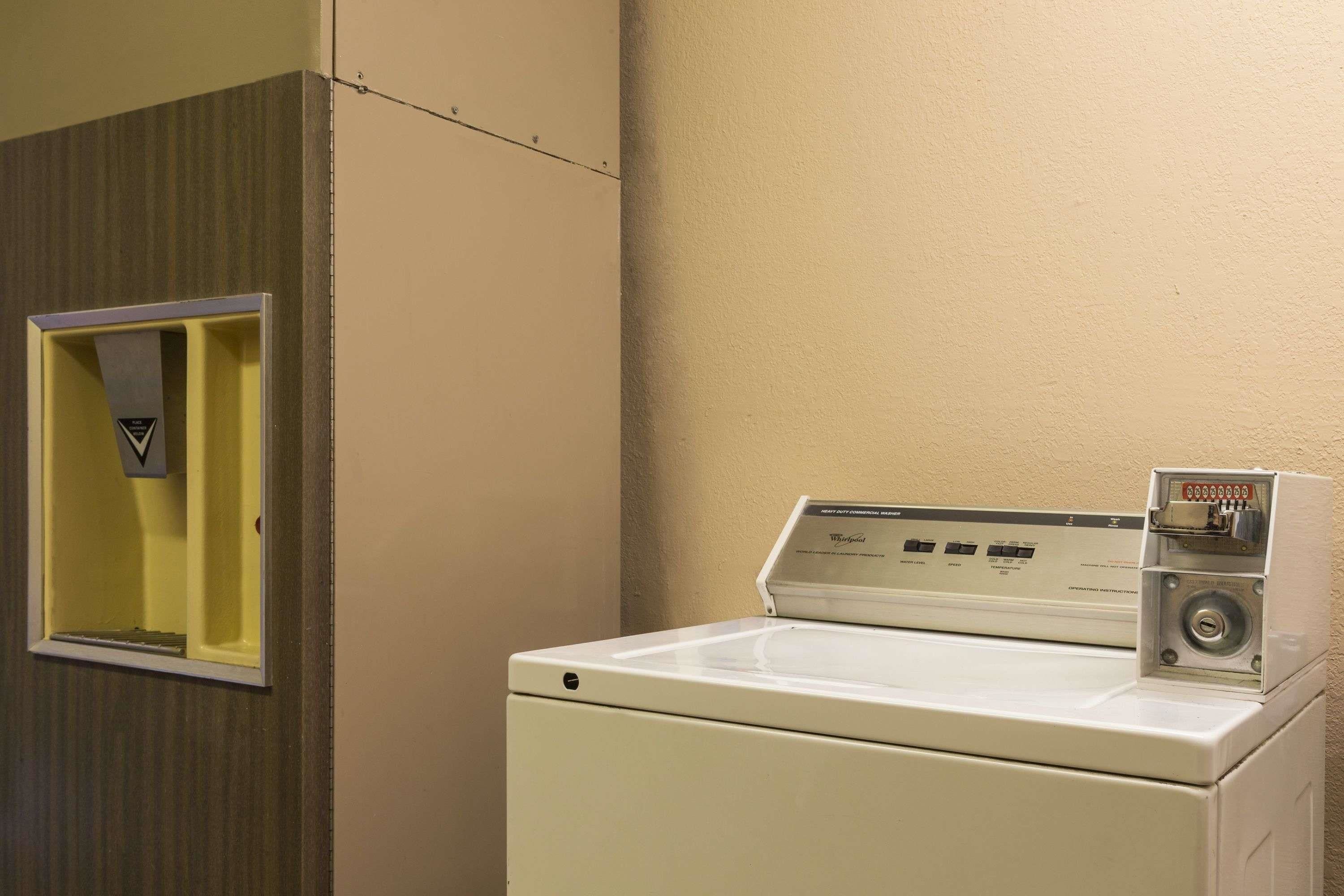 A front-loading white washer and dryer in a laundry room with a yellow door and a control panel on the right side.
