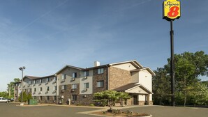 A multi-story hotel with a Super 8 sign, featuring a mix of brick and siding exterior, a parking lot, and a small landscaped area with a tree. - Super 8 by Wyndham Taylor/Detroit Area (Taylor)